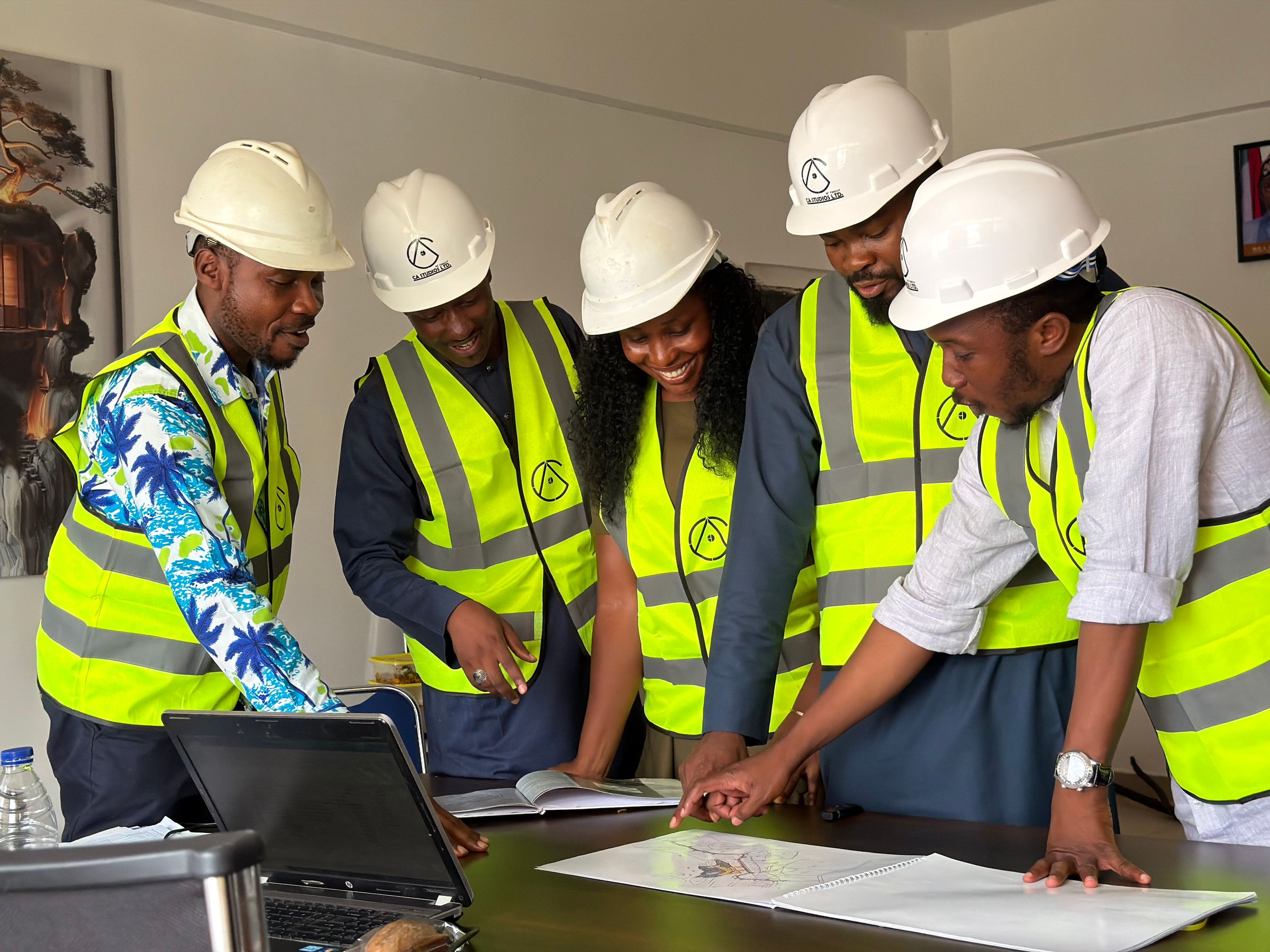 Team reviewing spiral-bound construction plans and a laptop around an office table.